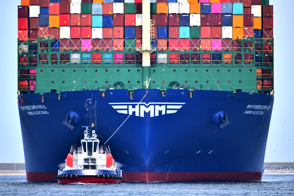 Schip met containers wordt door een sleeper de Rotterdamse haven in geloodst.